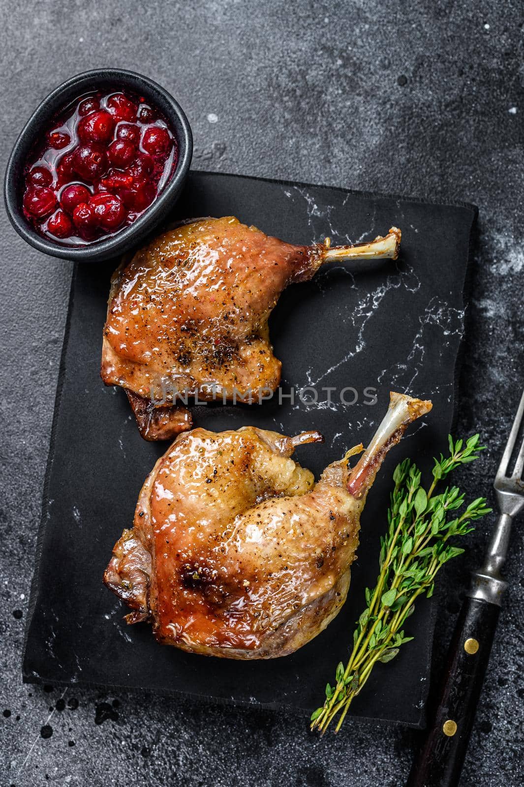 Roasted duck leg confit with cranberrie sauce. Black background. top view by Composter