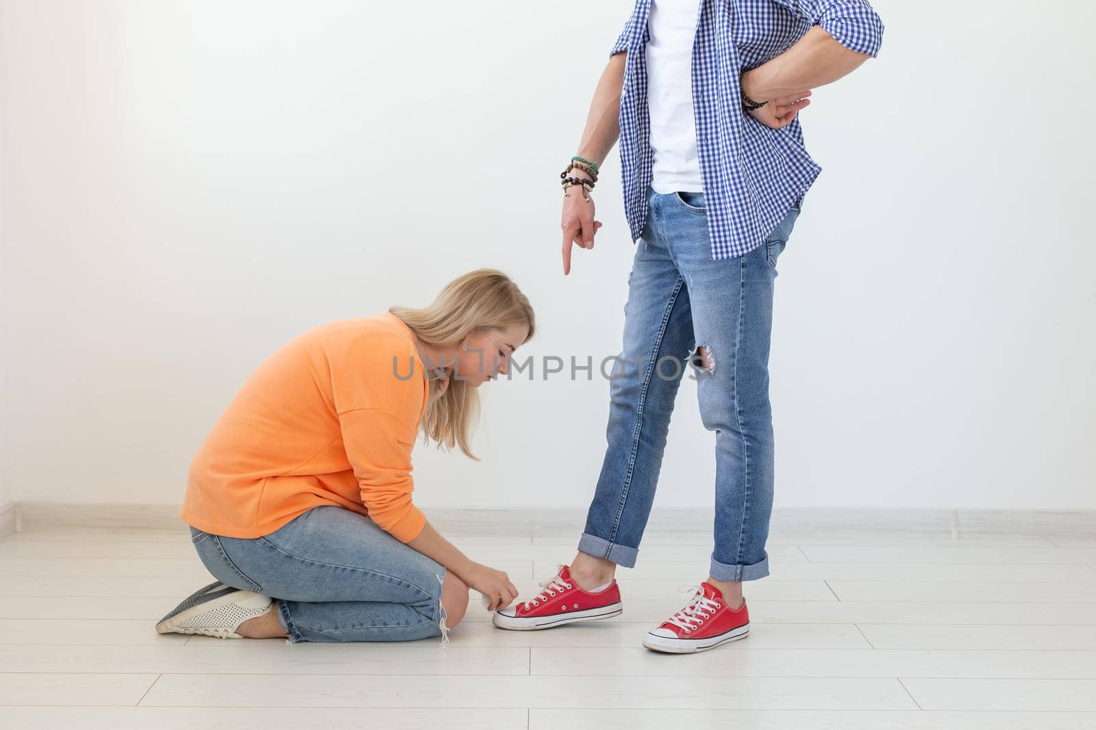 Young pretty blonde girl sits on her lap and touches the shoes of a joyful young man. Concept of unequal relationships and sexism. Copyspace