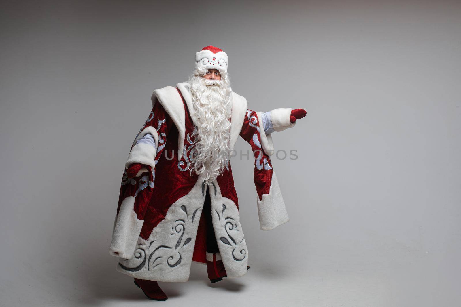 Stock photo of smiling happy Santa in traditional hat with rhinestones and long white beard looking at camera. Cutout on red background. Happiness concept.