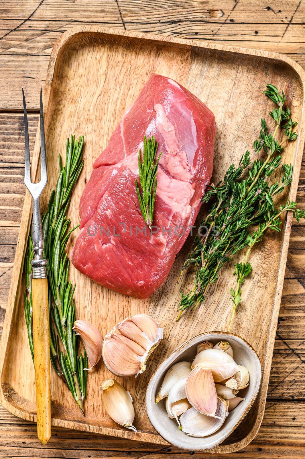 Raw lamb meat steak in a wooden tray with herbs. wooden background. Top view.