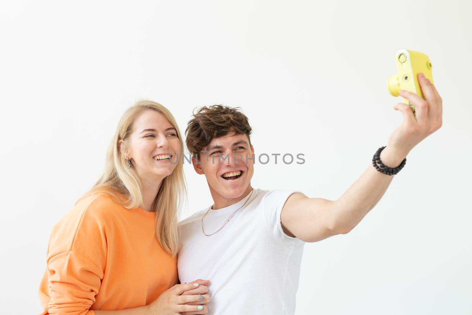 Funny young couple in love cute man and charming woman making selfie on vintage yellow film camera posing on a white background. Concept lovers of photography and hobbies. Advertising space