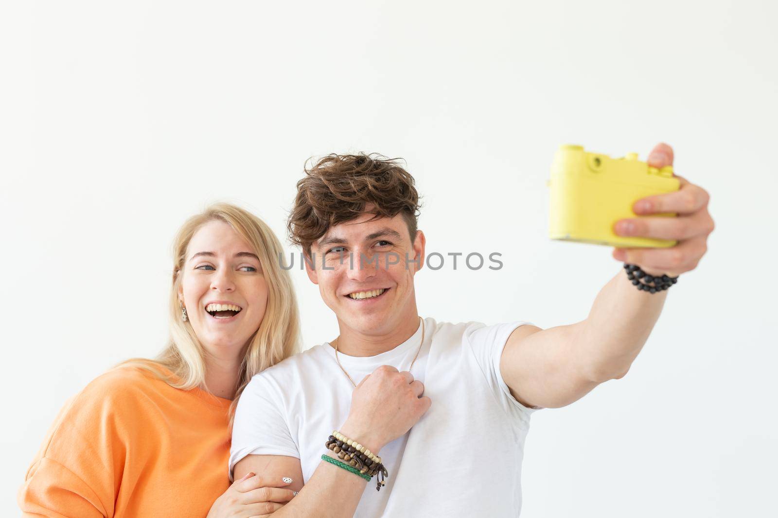 Funny crazy young couple blonde girl and a hipster guy taking a selfie on a vintage yellow film camera posing on a white background. Concept of photography hobby. Advertising space