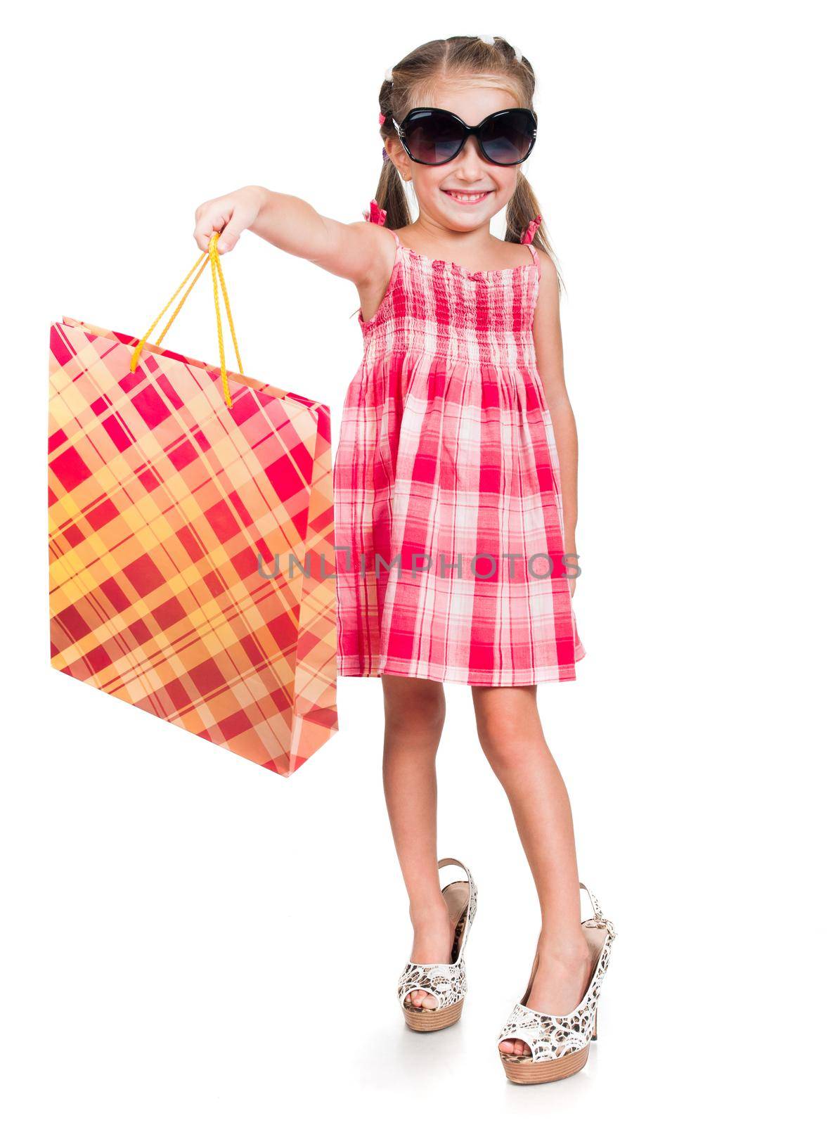 Smiling little girl in mother glasses and shoes with shopping bag isolated on a white background