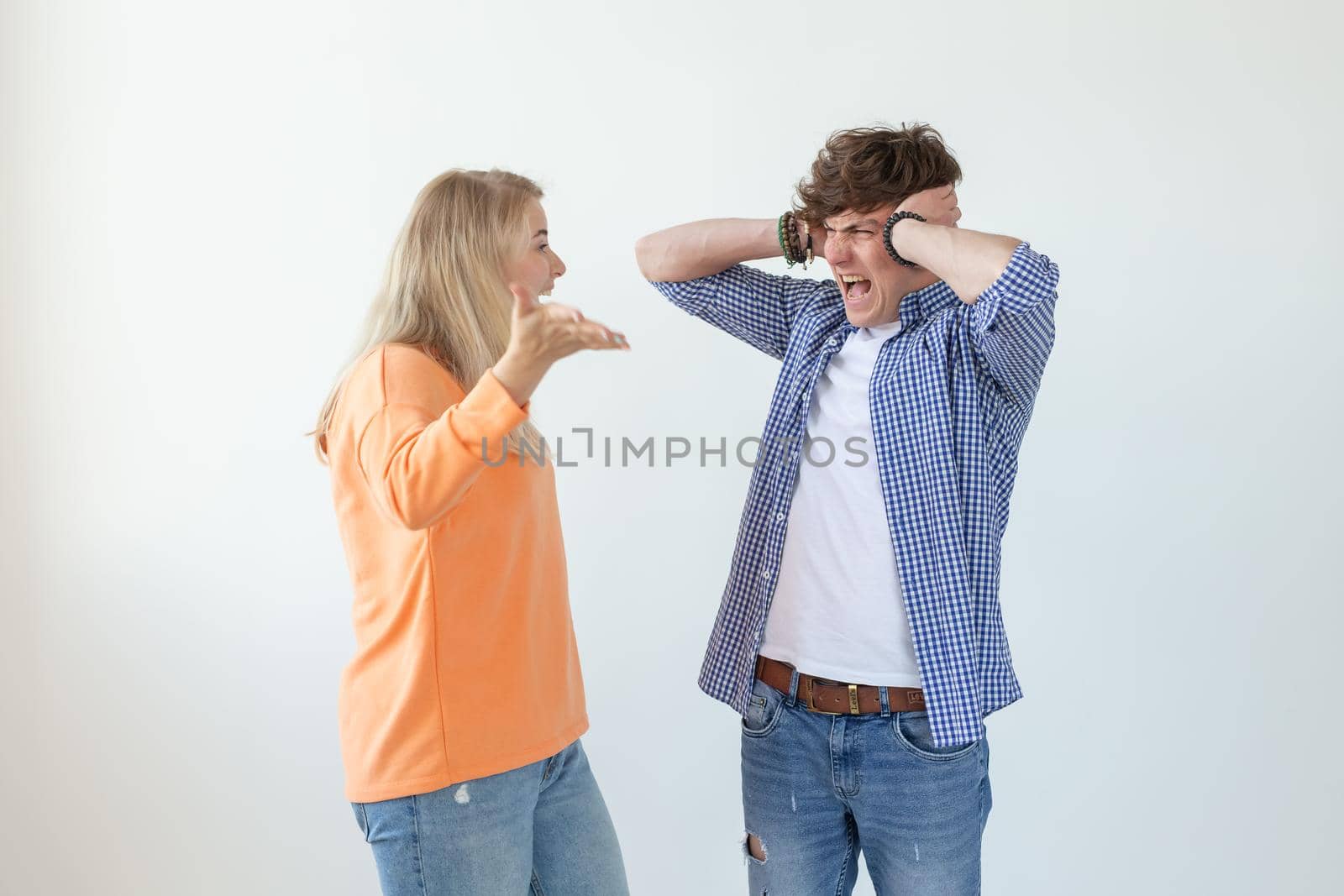 Young nervous couple wicked cute girl and upset young guy plugging ears cursing standing against white background. Misunderstanding and relationship crisis concept