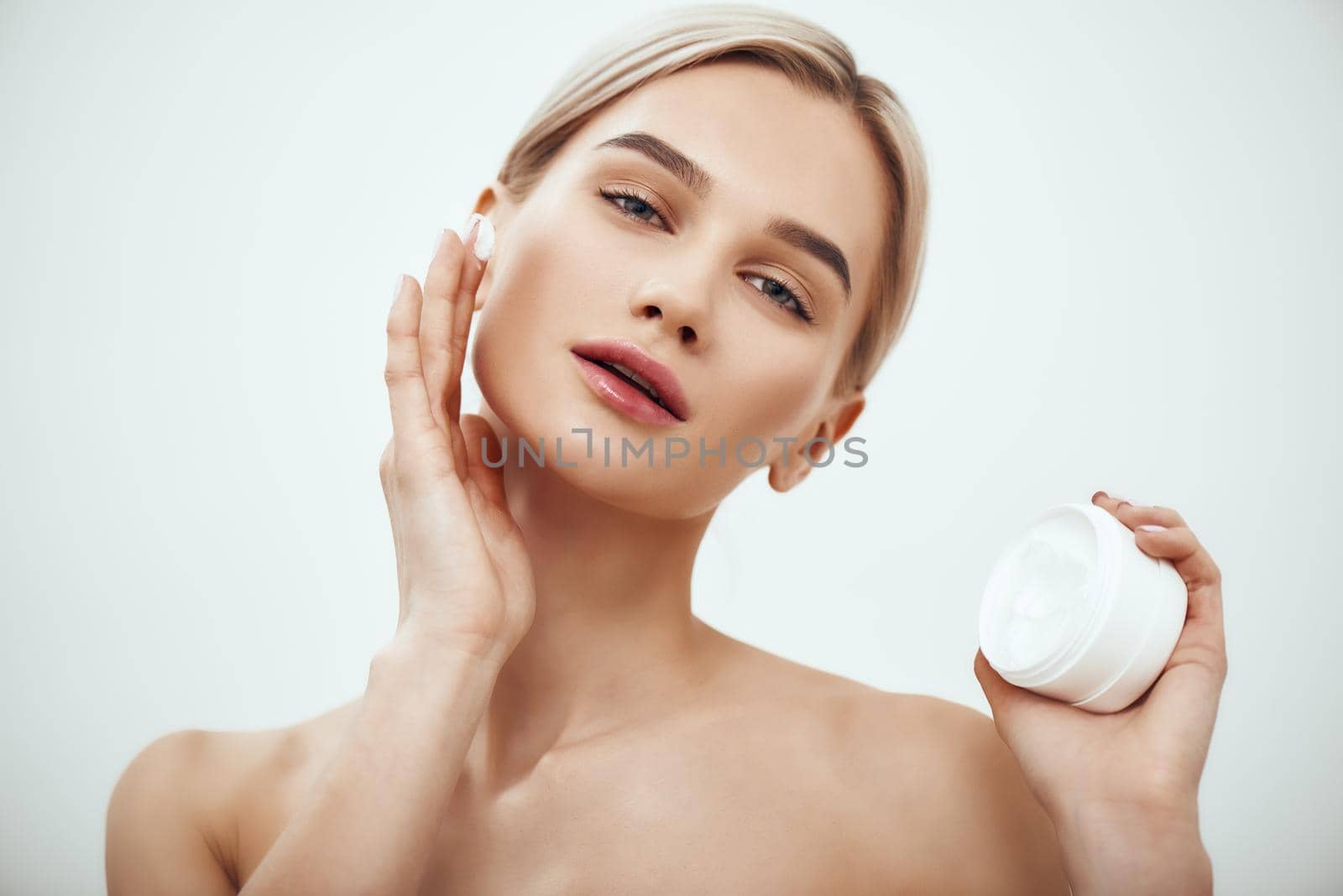 Best moisturizer for your skin type. Portrait of gorgeous young woman spreading cream on her face. Studio shot. Skin care. Beauty concept. Cosmetics concept