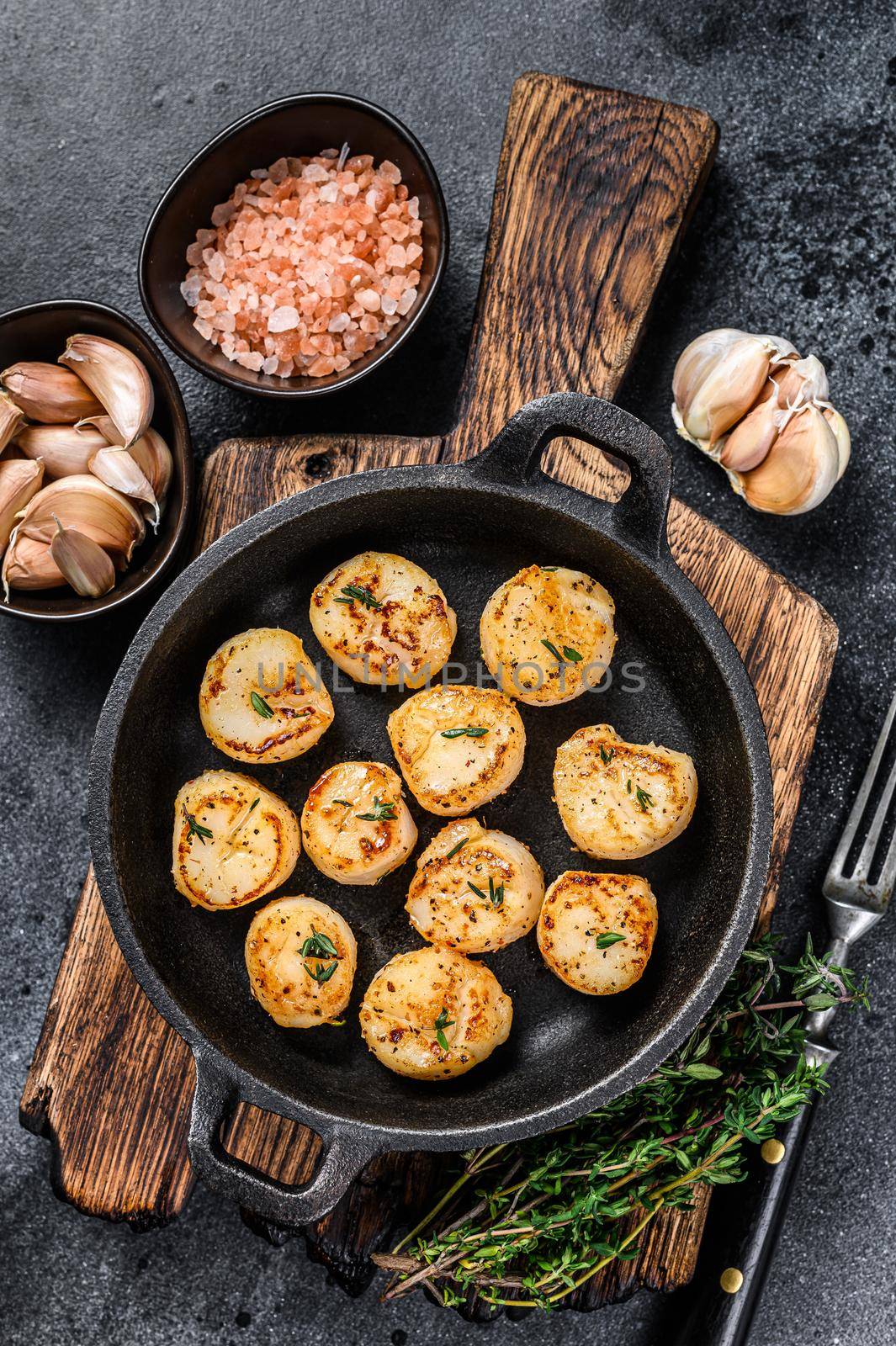 Fried scallops with butter sauce in a pan. Black background. Top view by Composter