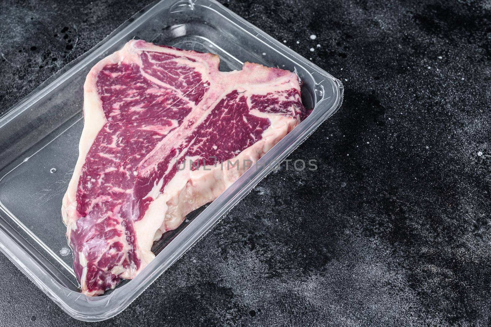 T-bon raw beef steak in vacuum packaging. Black background. Top view. Copy space by Composter