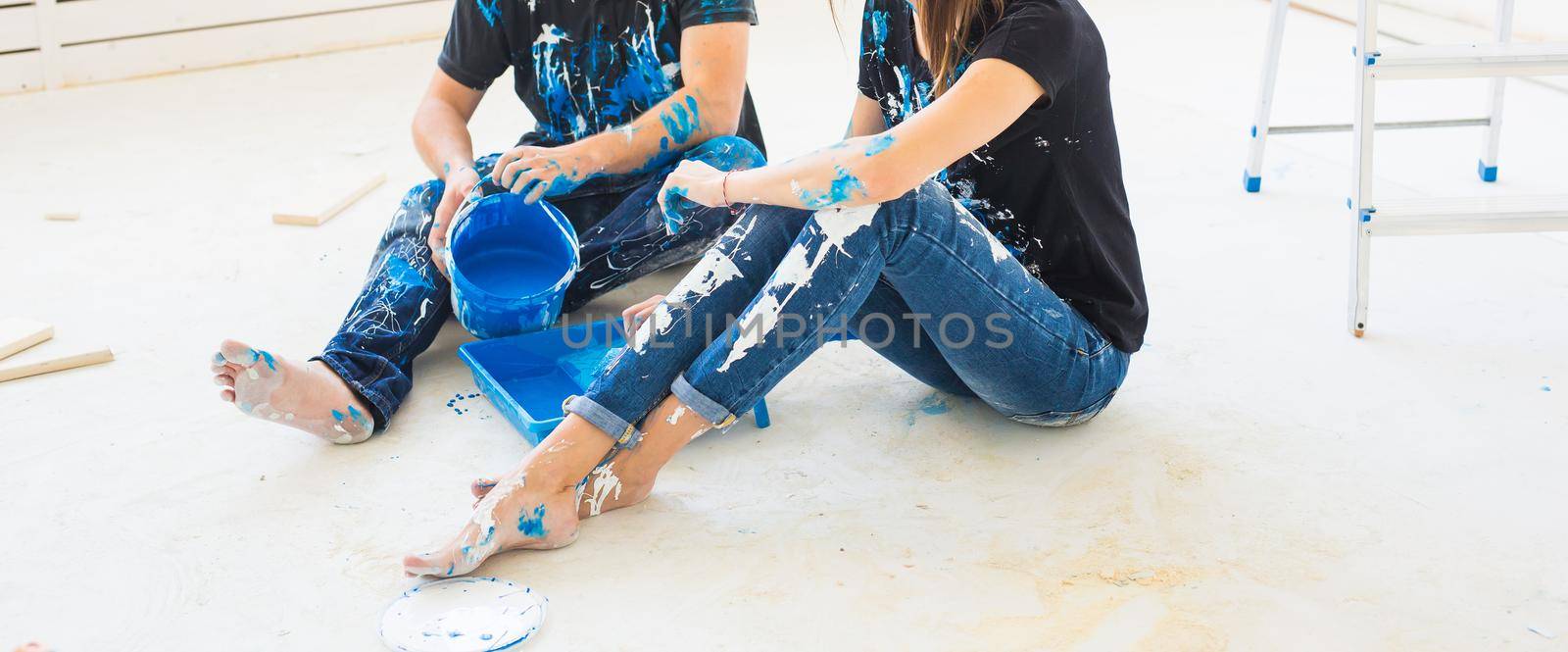 People and interiors concept - Young couple sitting on the white floor and pour paint.