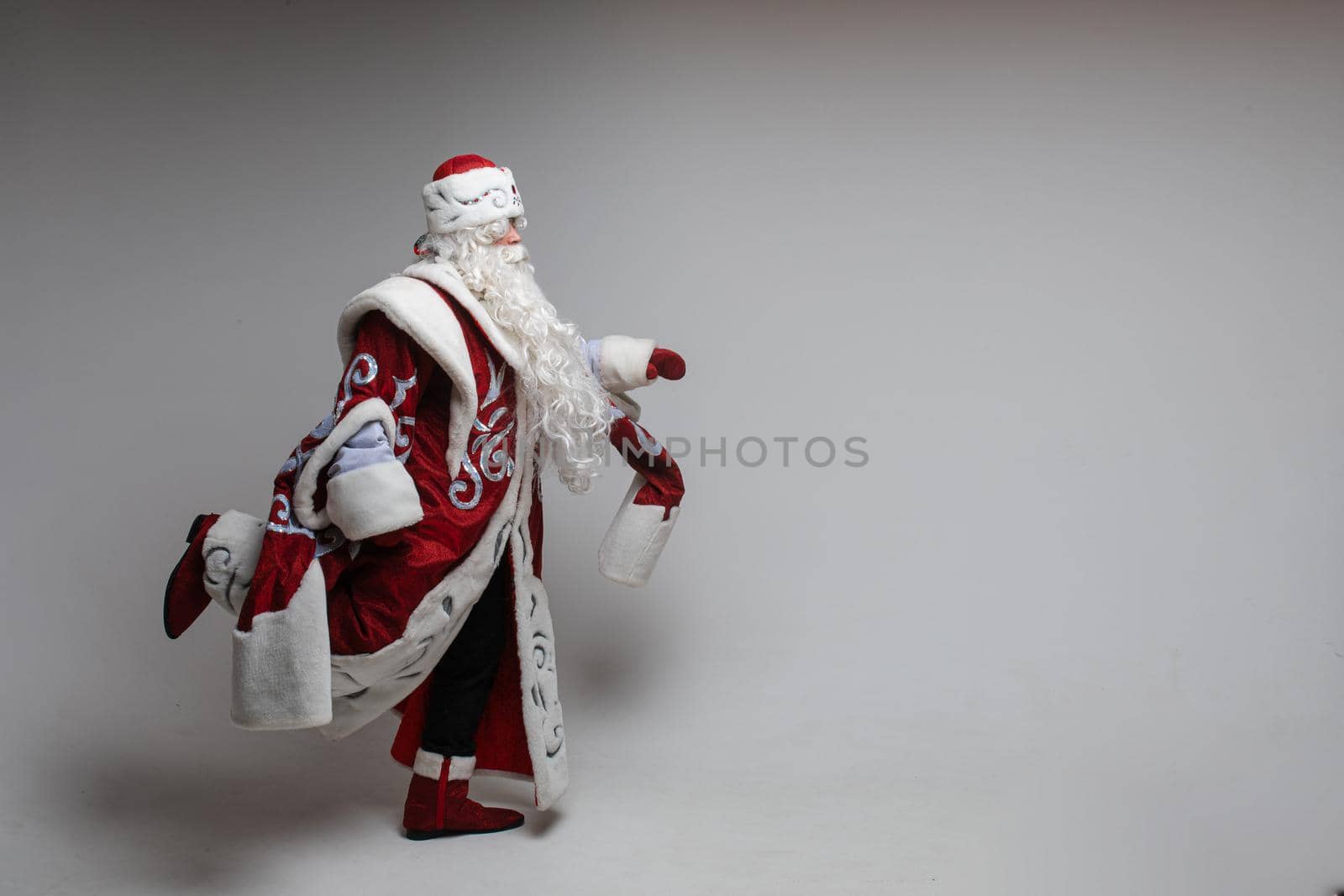 Full length portrait of Santa Claus with long beard wearing traditional costume running against grey background.