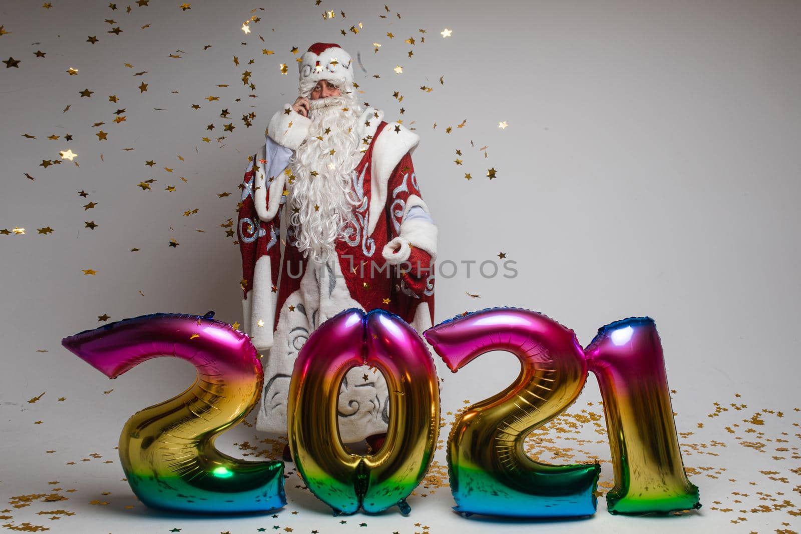 2021 new year celebration, santa claus with colorful balloons and confetti on gray studio background, copy space. High quality photo