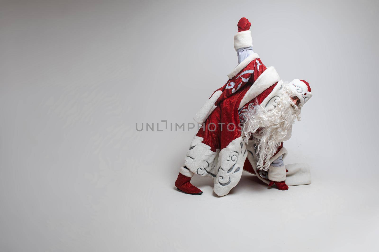 Stock photo of active Father Frost in traditional costume doing exercise in studio. Father Frost stretching or warming up before workout. Isolate.