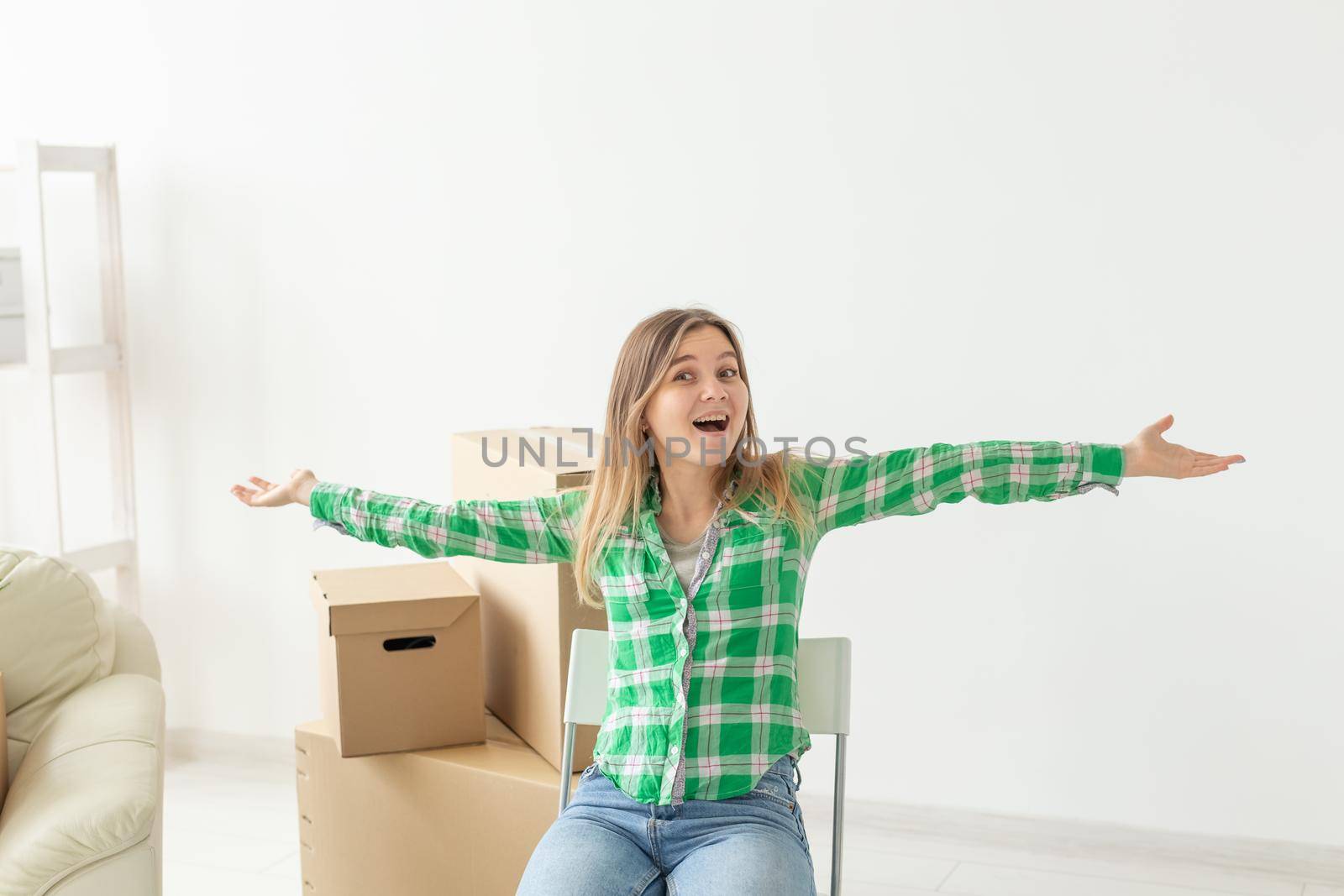 Charming young woman in casual clothes rejoices sitting on a chair among the boxes of things in her living room in a new apartment during the move. Concept of new housing and housewarming. Copyspace