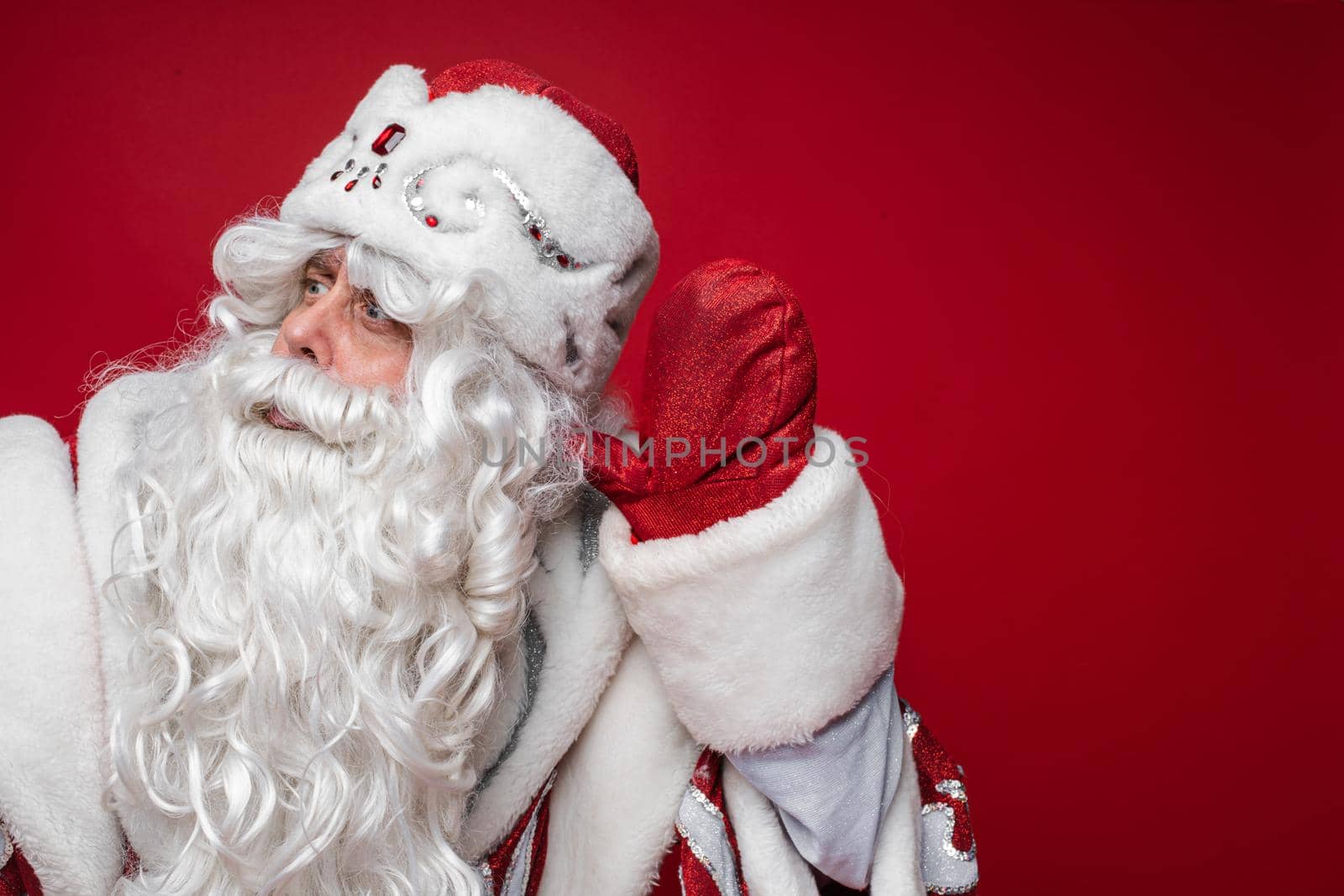 santa claus with long white beard tries to hears someone, picture isolated on red background