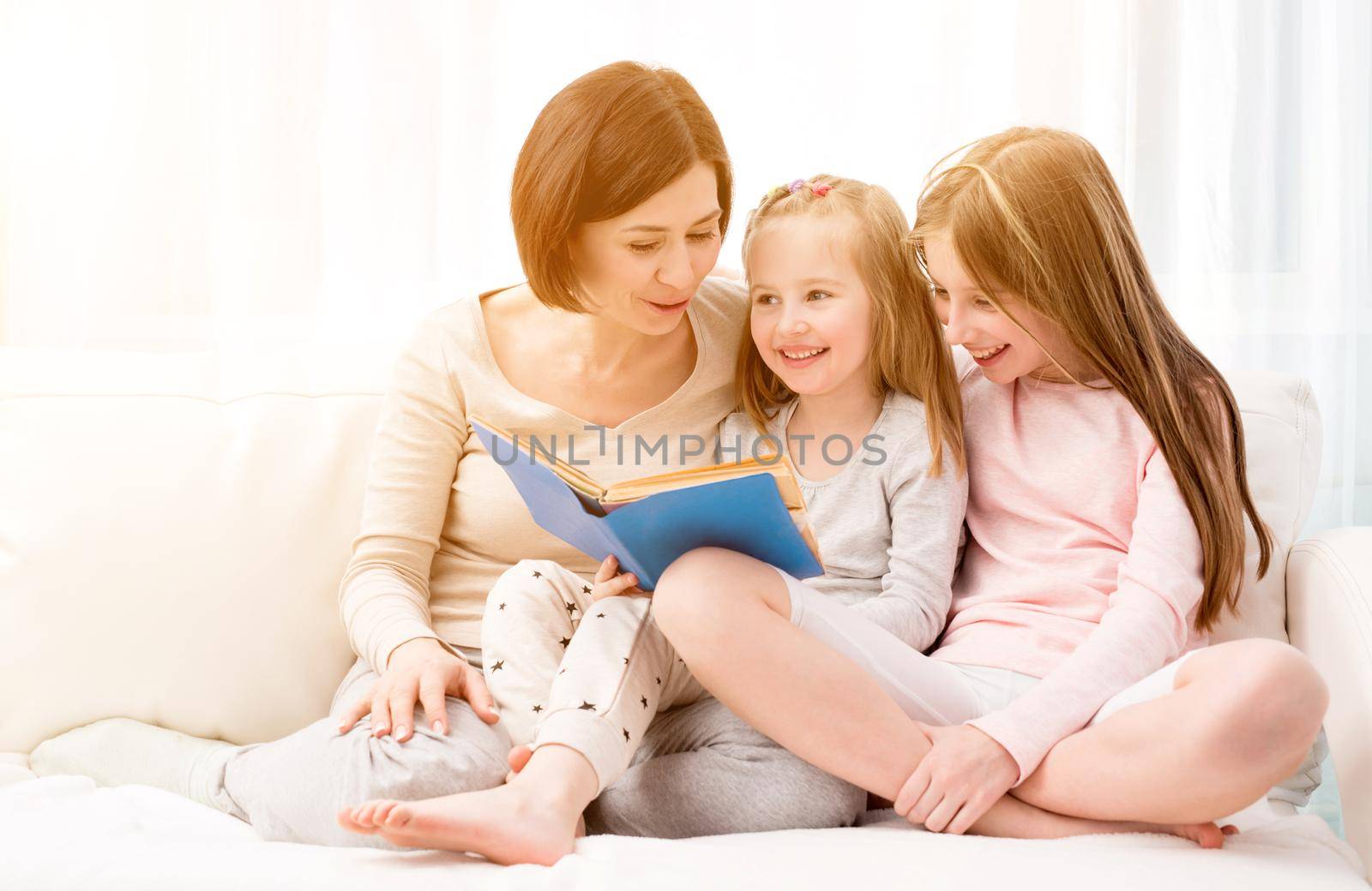 Mom and her two little daughters reading children's book in the living room. Mom and daughters sitting on the coach and reaading