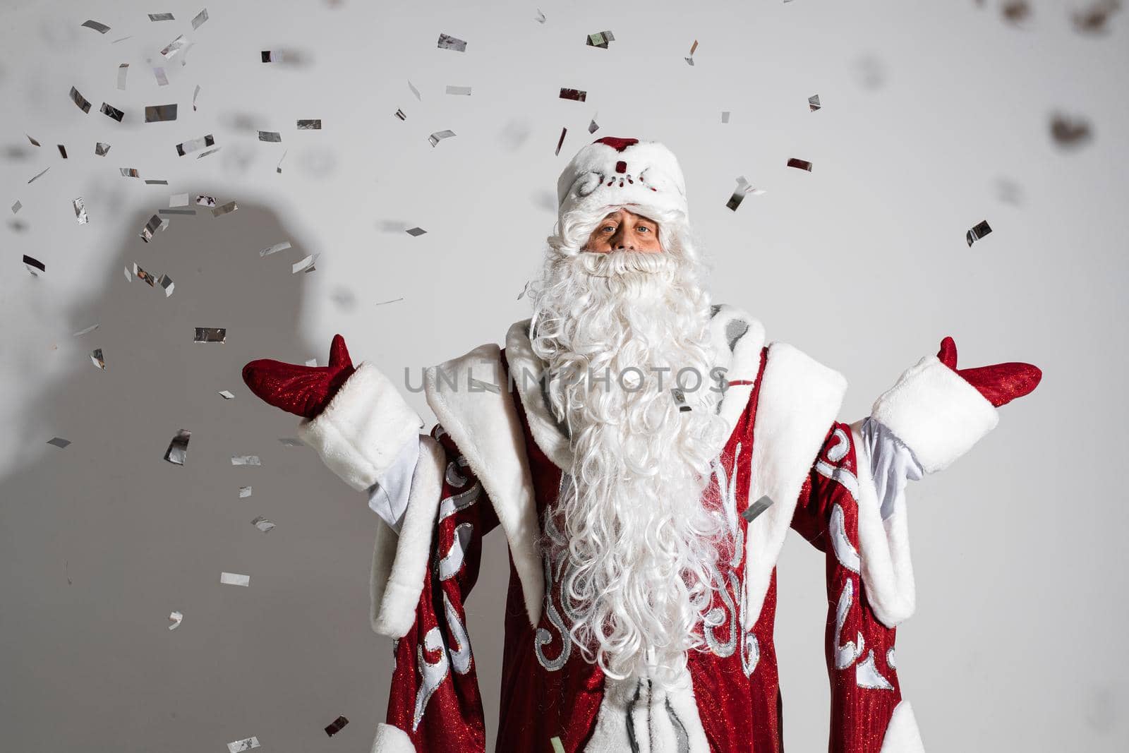 Santa claus under festive xmas confetti showing welcome gesture, studio holiday portrait for congratulations . High quality photo