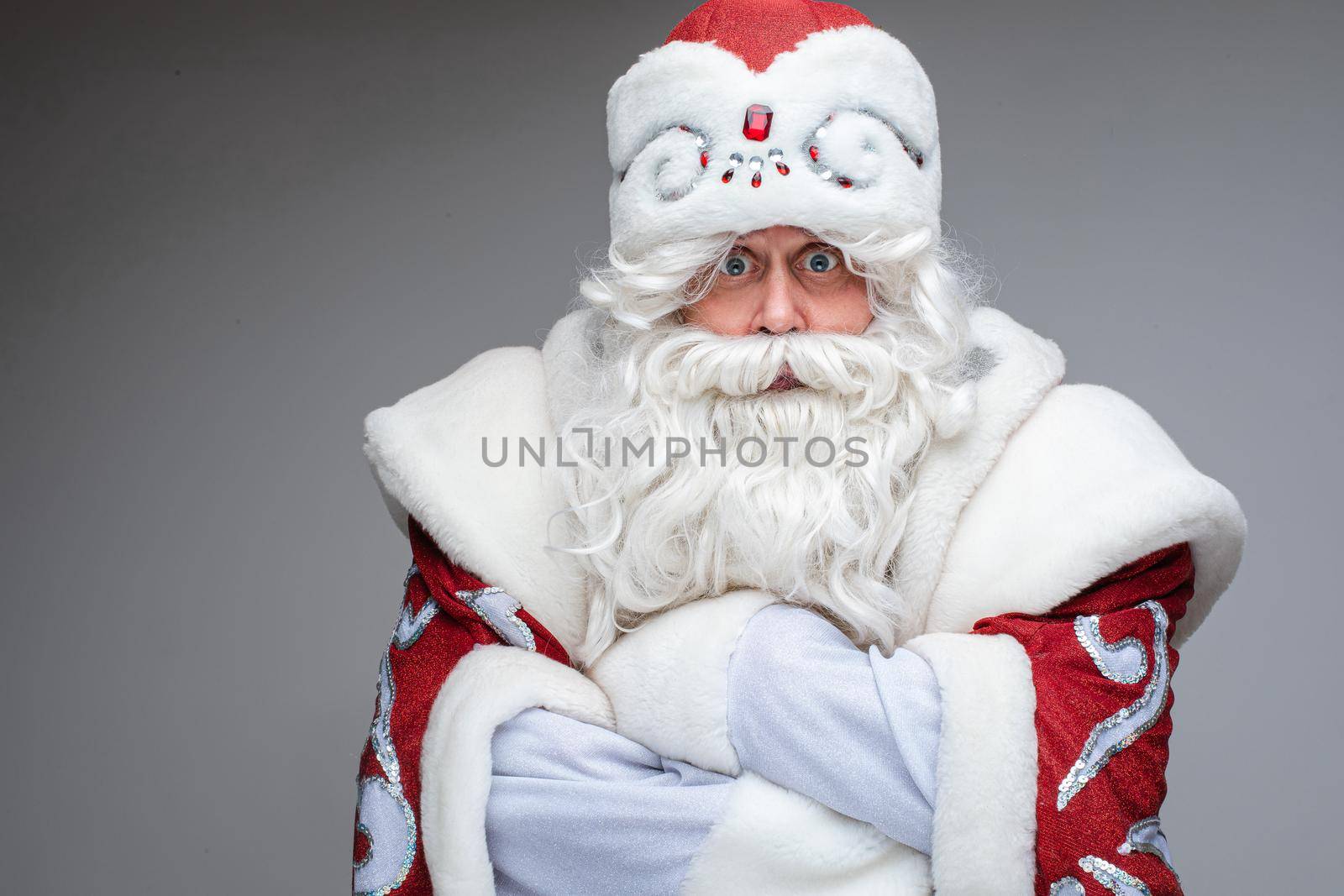 Stock photo of unhappy or displeased Father Frost in traditional fancy costume looking at camera with wide eyes and crossed arms. Strike concept.