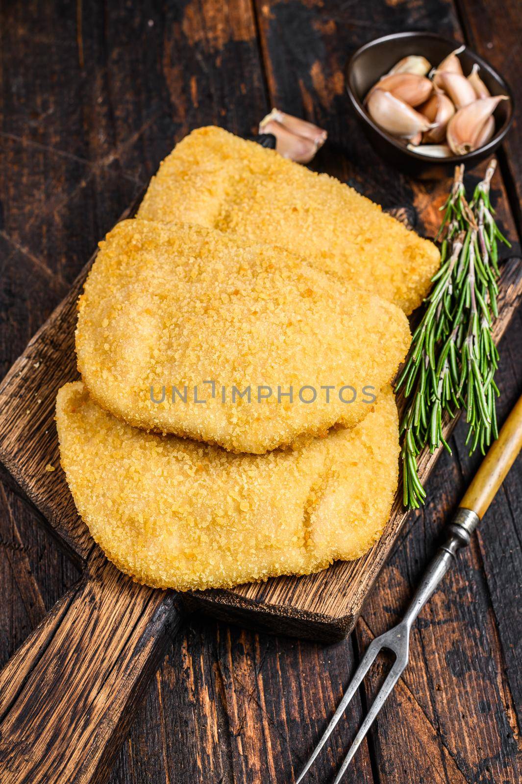 Raw chicken cordon bleu meat cutlets with bread crumbs on a wooden board. Dark wooden background. Top view.