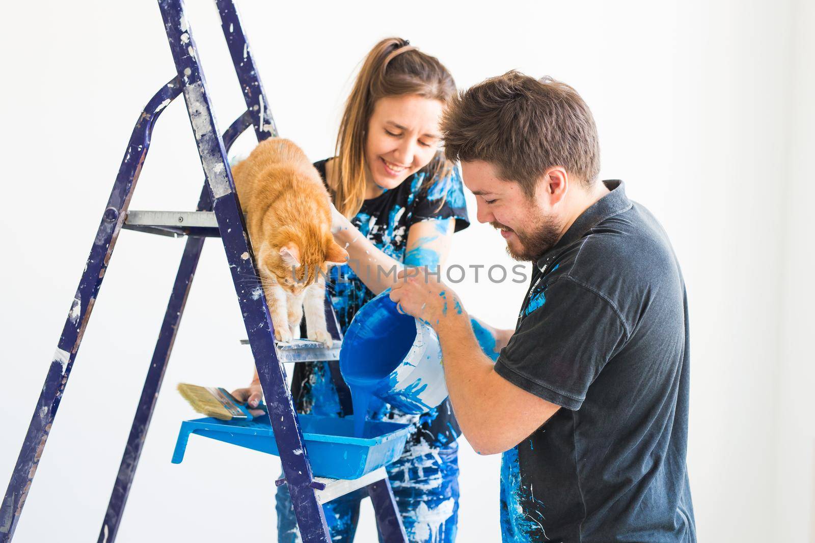 People, redecoration and renovation concept - portrait of couple with cat pour paint.