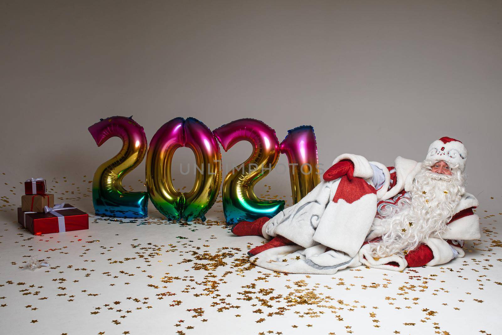 father frost lies near the baloons with numbers 2021 and christmas presents, isolated on white background