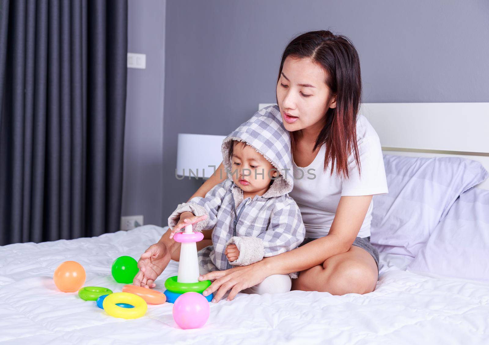 baby playing toys with mother on bed at home