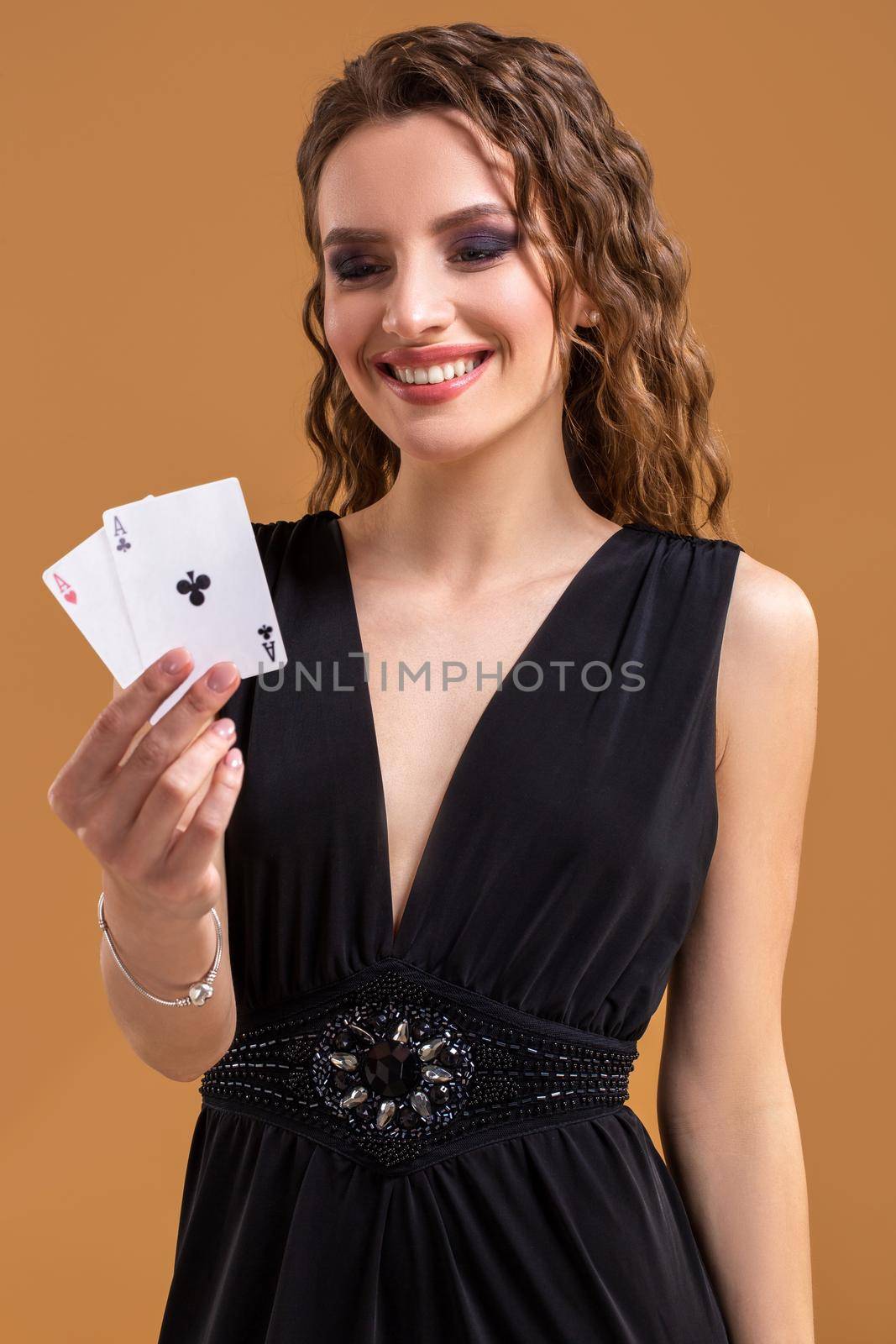 Beautiful caucasian woman in black dress with poker cards gambling in casino. Studio shot on a beige background