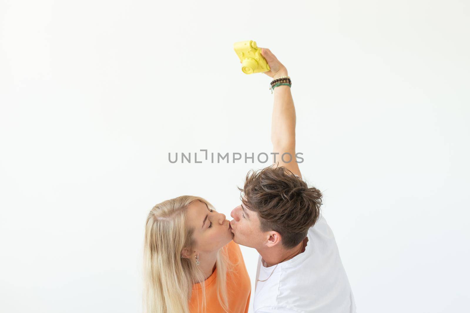 Funny young couple in love cute man and charming woman making selfie on vintage yellow film camera posing on a white background. Concept lovers of photography and hobbies. Advertising space