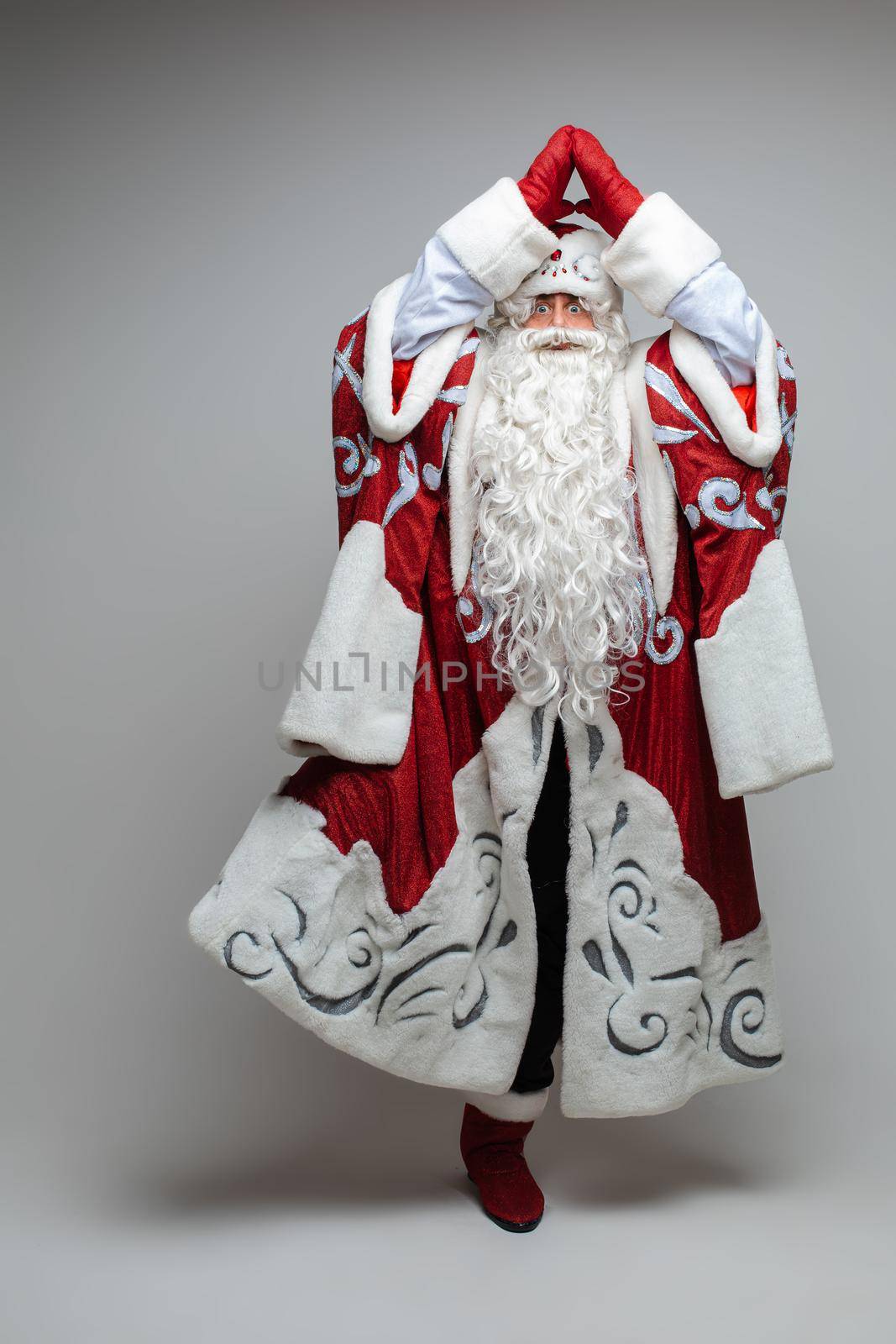 Stock photo of smiling happy Santa in traditional hat with rhinestones and long white beard looking at camera. Cutout on red background. Happiness concept.