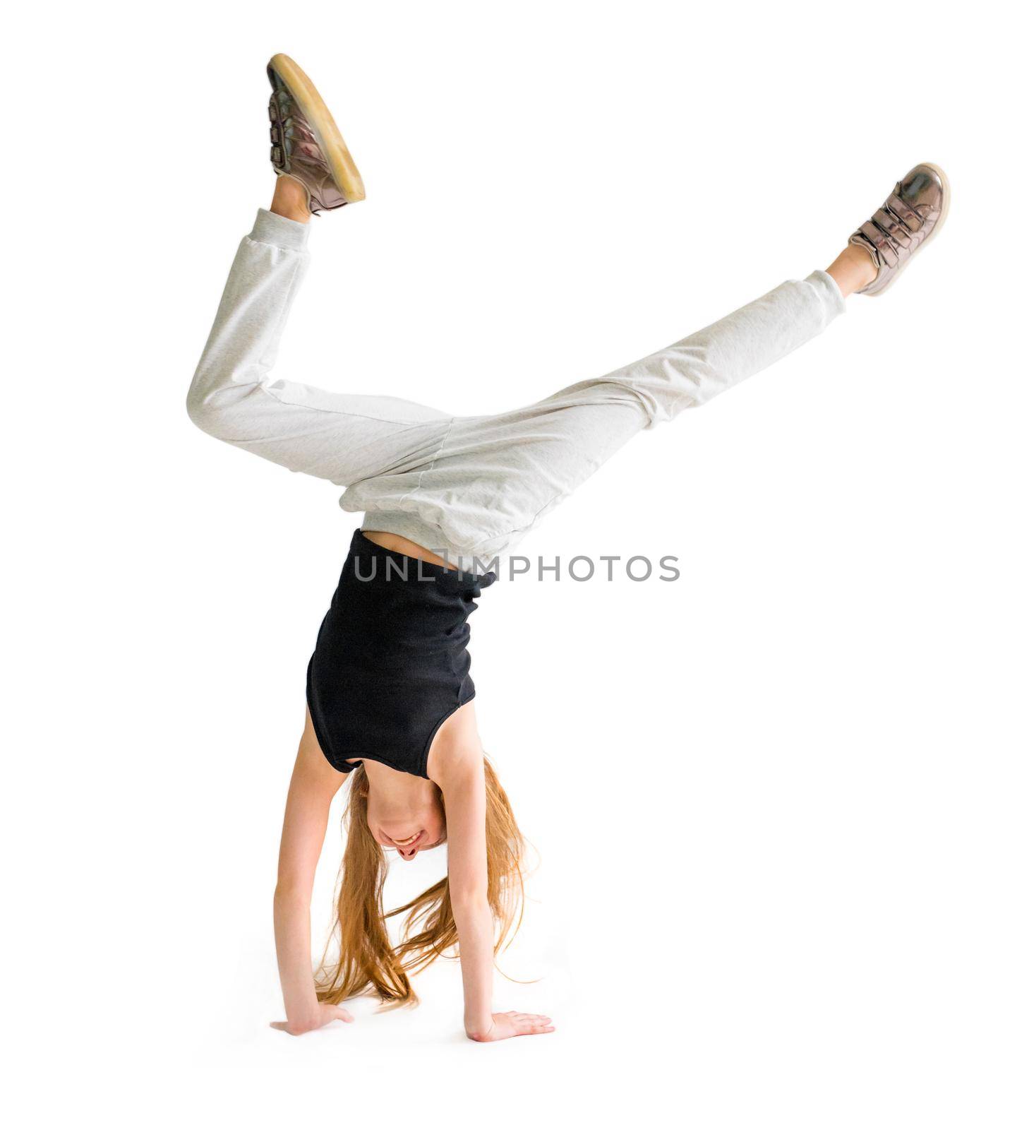 Attractive flexible teenage girl doing handstand on light background