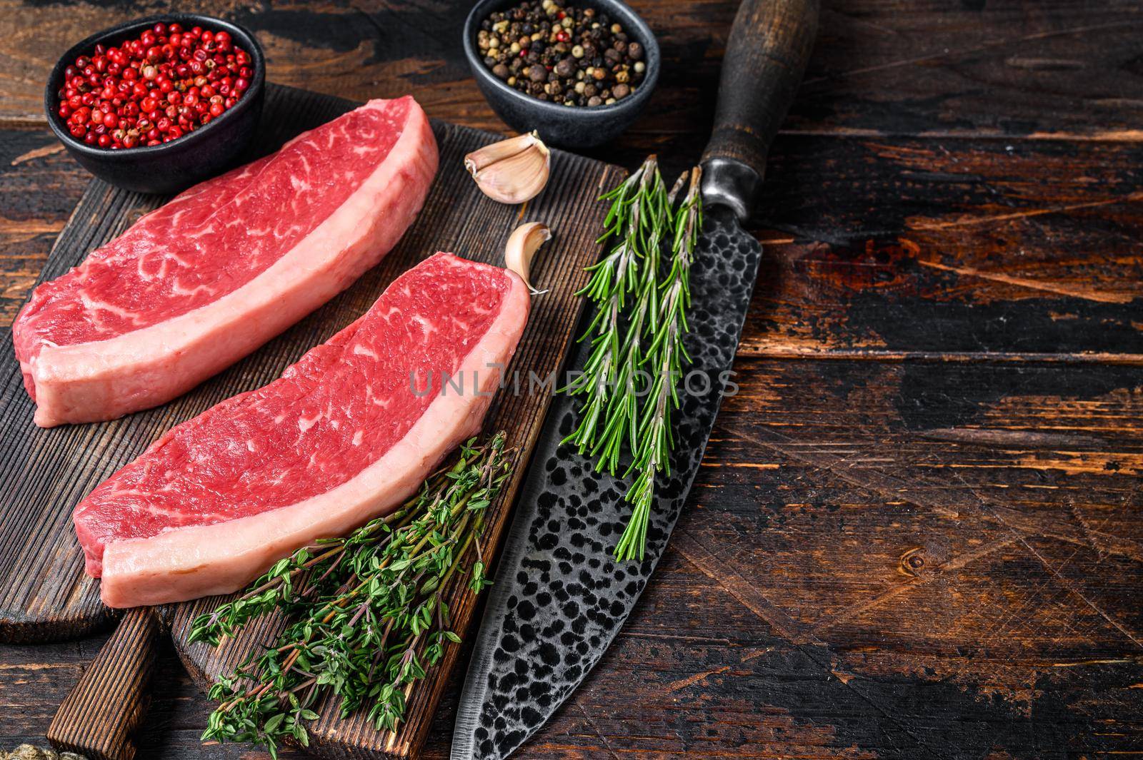 Raw top sirloin beef meat steak on a cutting wooden board. Dark wooden background. Top view. Copy space by Composter
