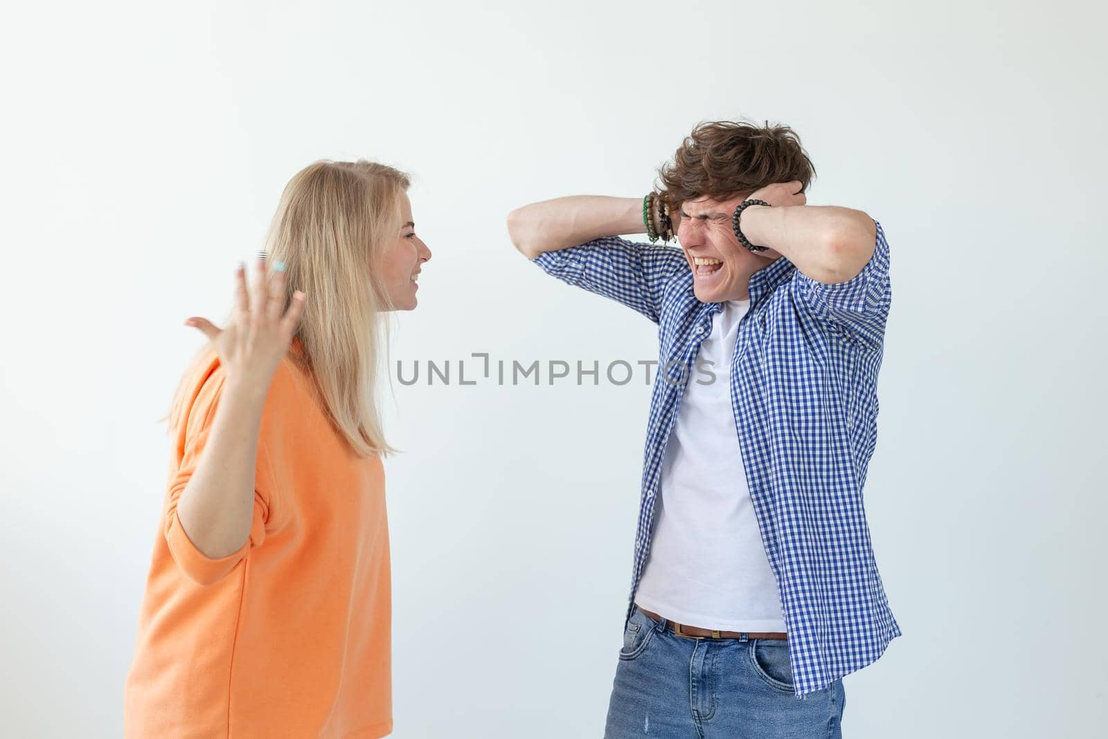 Young nervous couple wicked cute girl and upset young guy plugging ears cursing standing against white background. Misunderstanding and relationship crisis concept. by Satura86