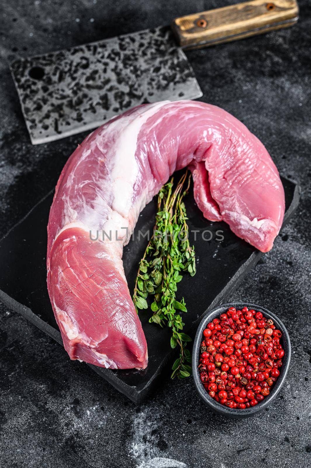 Raw pork tenderloin meat on a marble board. Black background. Top view.