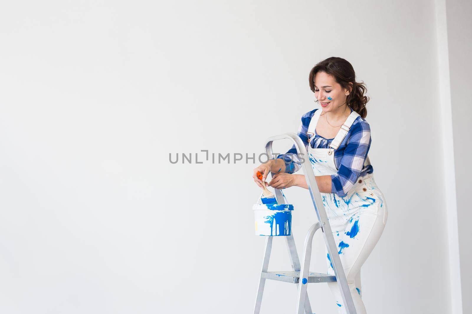 Repair, renovation, worker and people concept - Beautiful woman standing on the ladder and mixing paint over white background with copy space.
