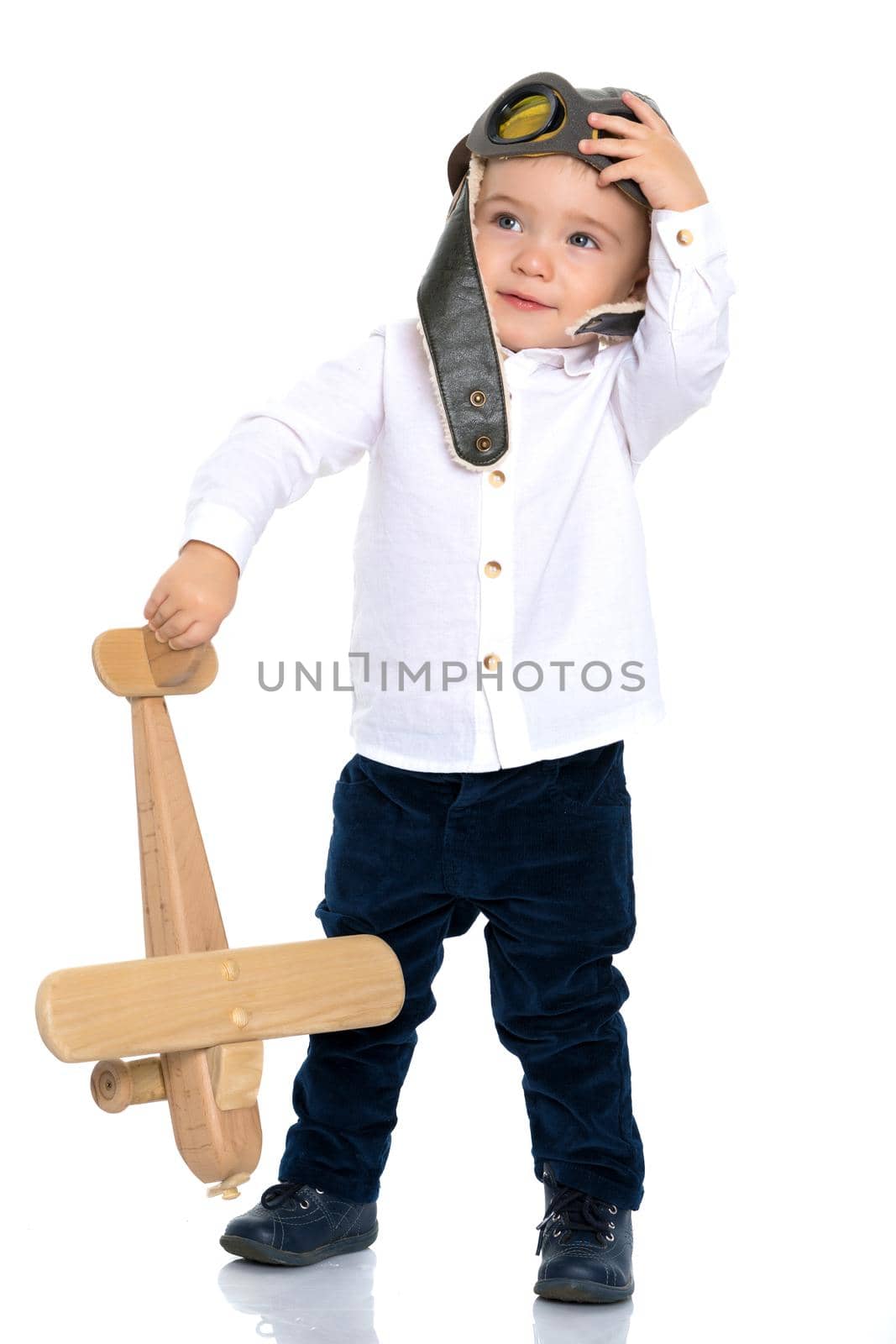 The boy in the helmet of the pilot plays with a toy wooden plane. He dreams of becoming a pilot. Concept of happy childhood, child in the family.Isolated on white background.