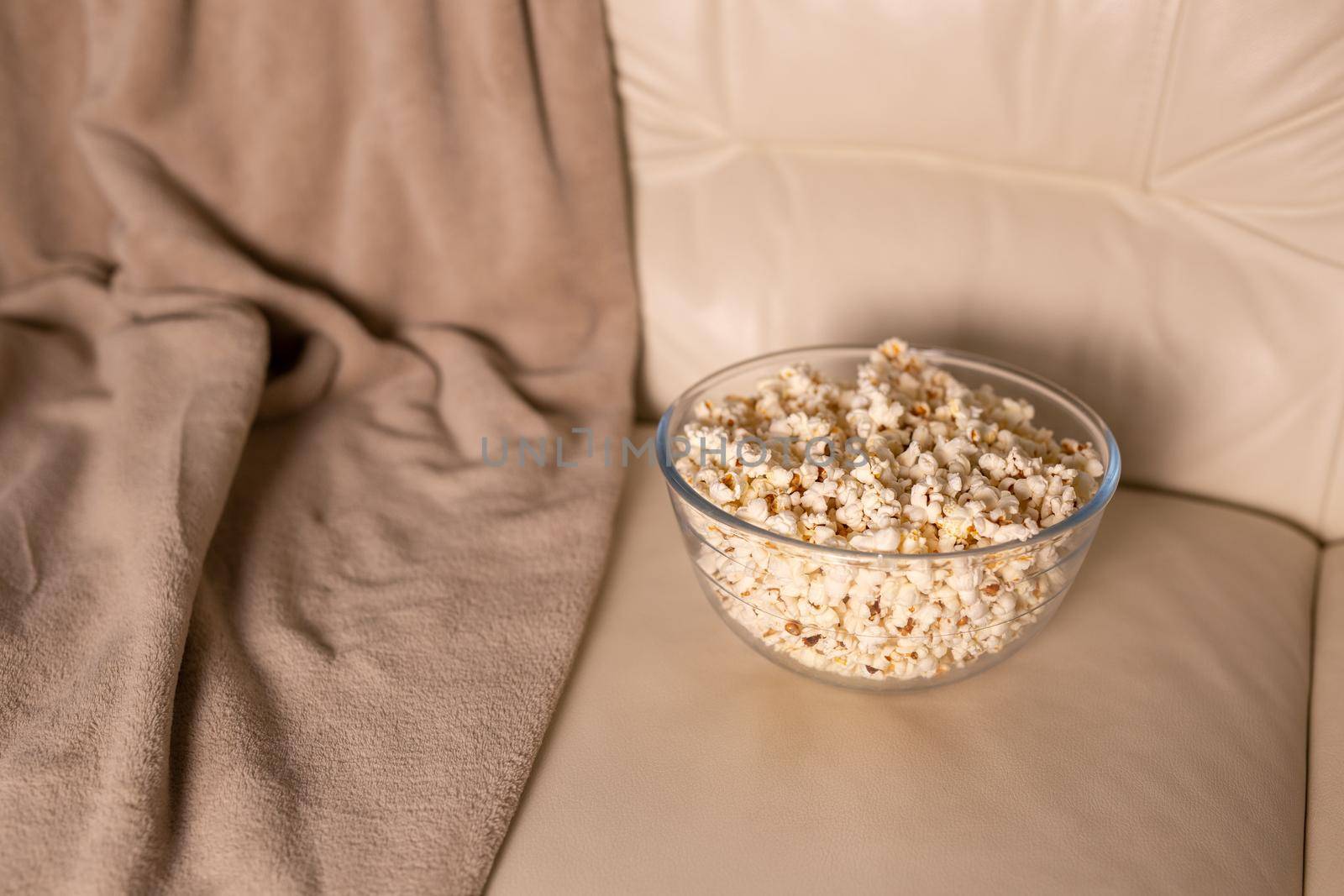 Bowl of popcorn for watching a film on a beige couch. Snacks and unhealthy junk food.