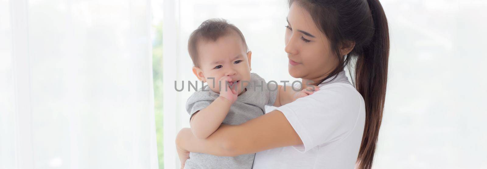 Young asian mother holding little baby girl and walking together in the bedroom at home, mom carry daughter and care, relationship of parent and child, toddler and parent, indoor, family concept. by nnudoo