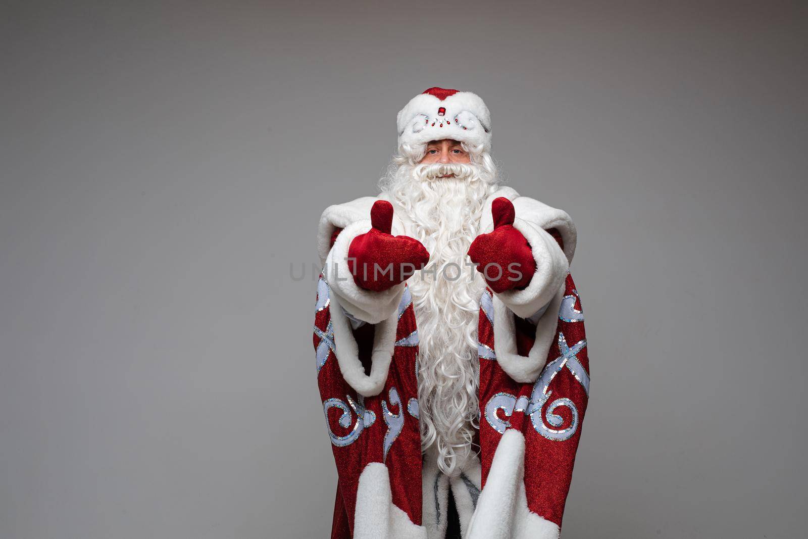 Stock photo of calm Father Frost with long white beard in traditional red and white costume holding both thumbs up.