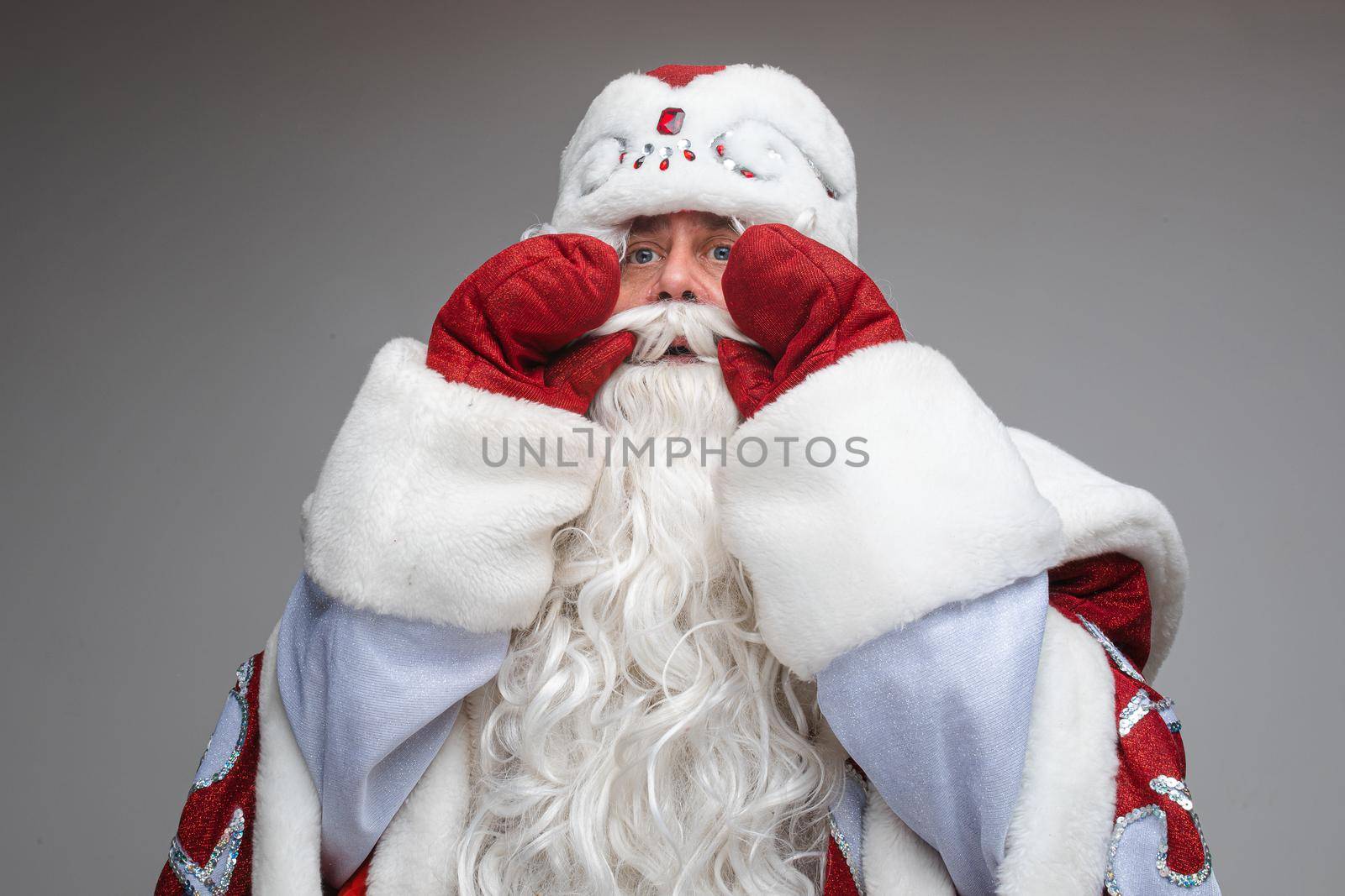 Santa Claus put on hands to mouth to ask or congratulate somebody, studio festive portrait on gray background. High quality photo