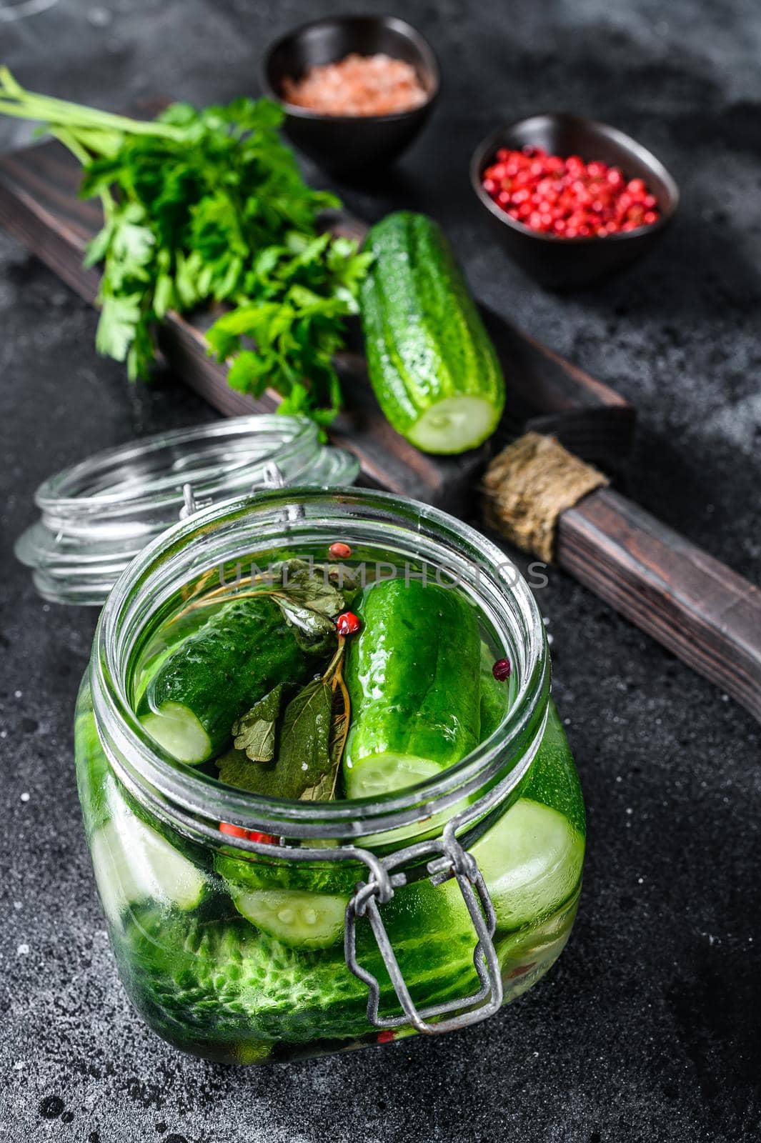 Green pickle cucumbers in a glass jar. Natural product. Black background. Top view by Composter