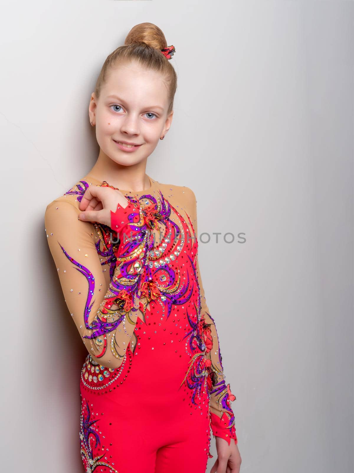 Little girl gymnast in a beautiful suit for competitions, posing in the studio near the wall. The concept of youth sports fashion, healthy lifestyle.