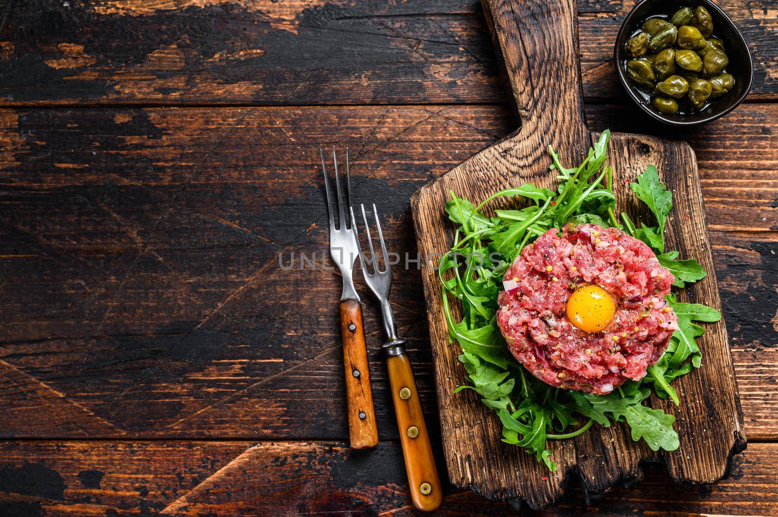 Tartar beef with a quail egg and arugula served on a cutting board. Dark wooden background. Top view. Copy space.