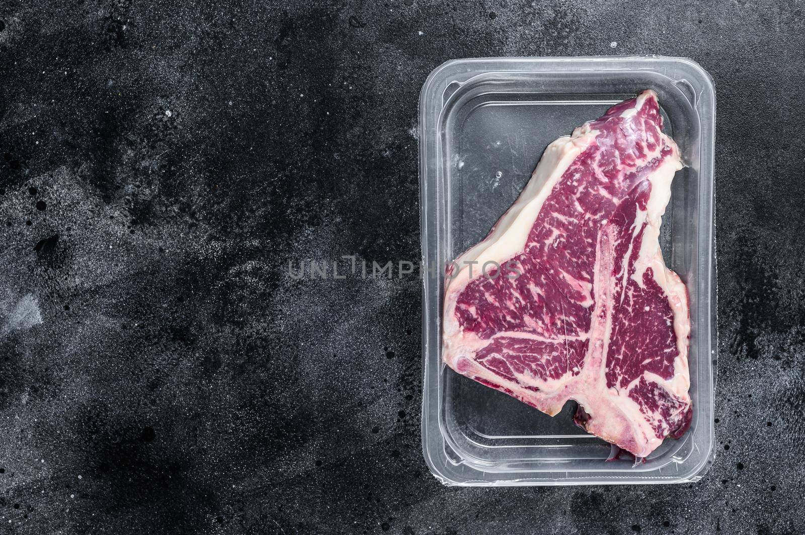 T-bon raw beef steak in vacuum packaging. Black background. Top view. Copy space.