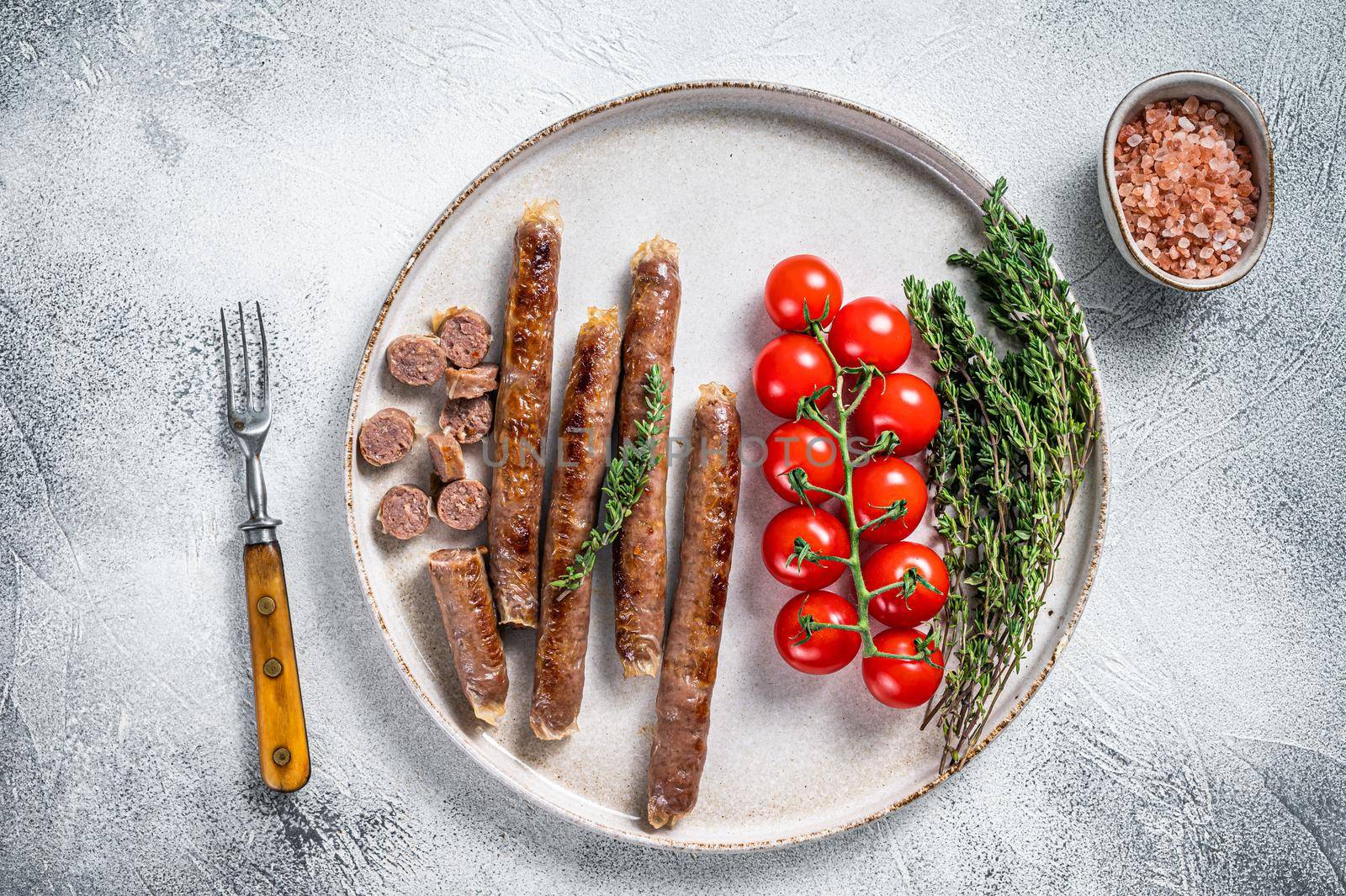 Grilled lamb meat sausage on a plate with herbs and tomato. White background. Top view.