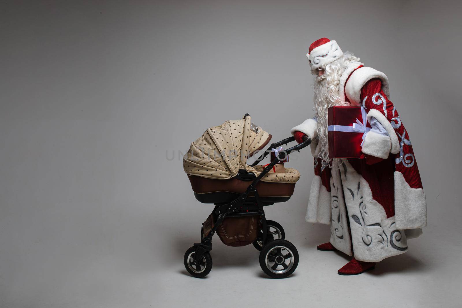 father frost walks with a little baby in the stoller, picture isolated on grey background