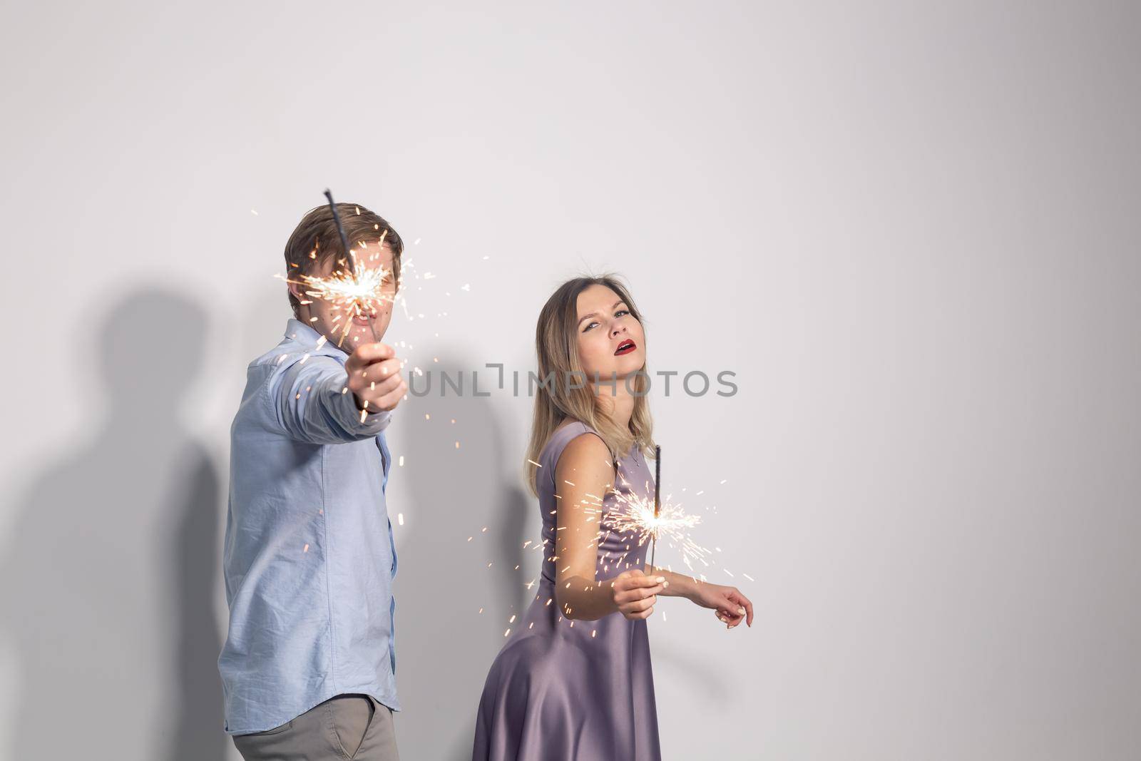 Holidays, party and celebrations concept - young couple with sparklers on white background.