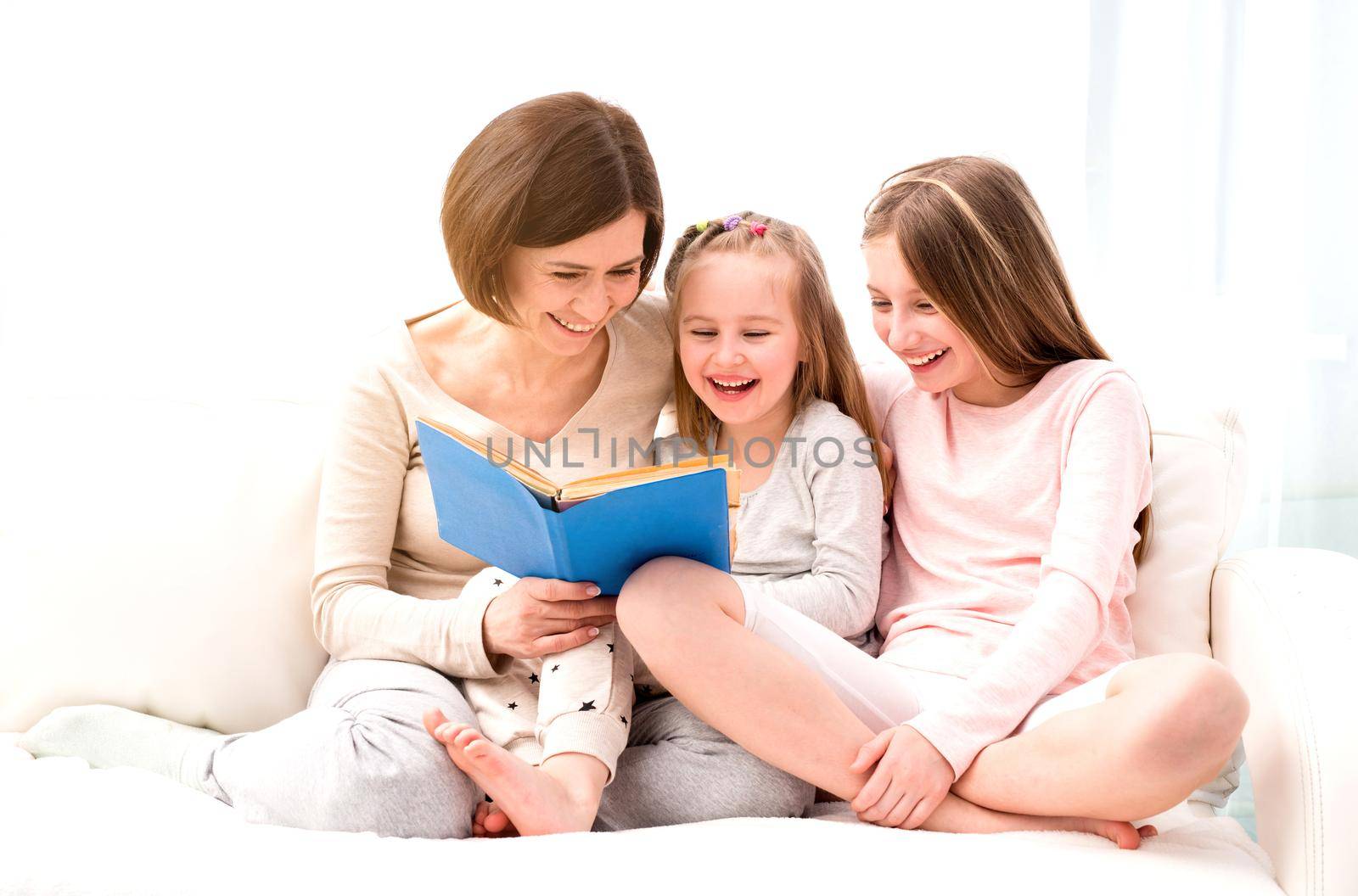 Mom and her two little daughters reading children's book in the living room. Mom and daughters sitting on the coach and reaading