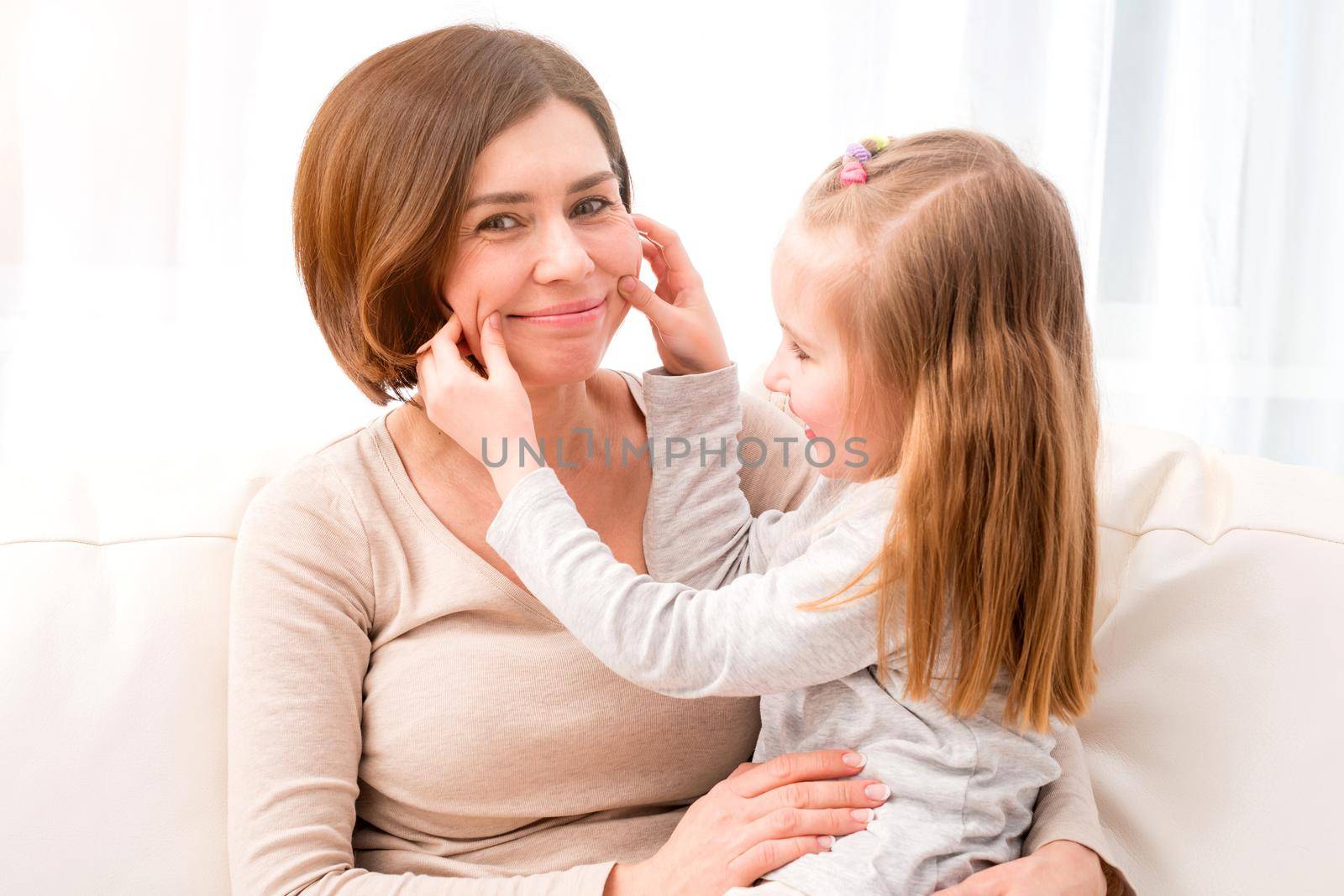 Mother and little daughter smiling. Pretty girl making her mother smile. Daughter and mom having fun together