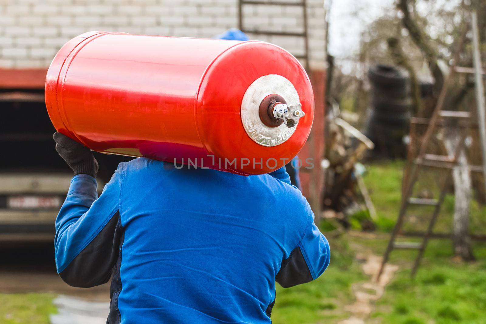 A male industrial worker walks with a gas cylinder to a gas car. Transportation and installation of a propane bottle to residential buildings.