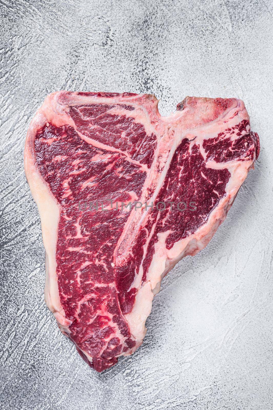 Raw T-bone or porterhouse Steak on kitchen table. White background. Top view.