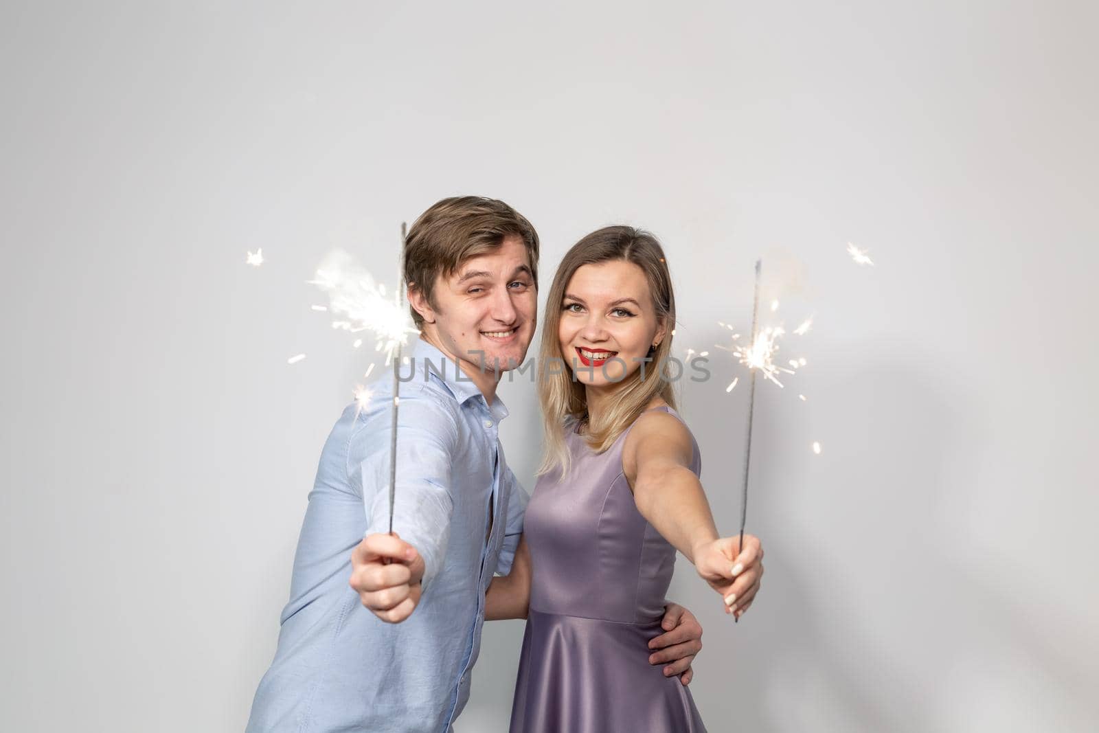 Party, celebration, event and holidays concept - man dressed in blue shirt and woman dressed in purple dress hold a firework stick.
