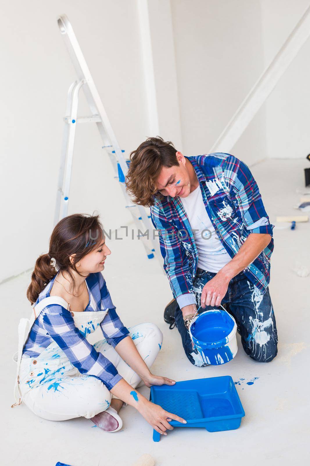 People and interiors concept - Young couple sitting on the white floor and pour paint.